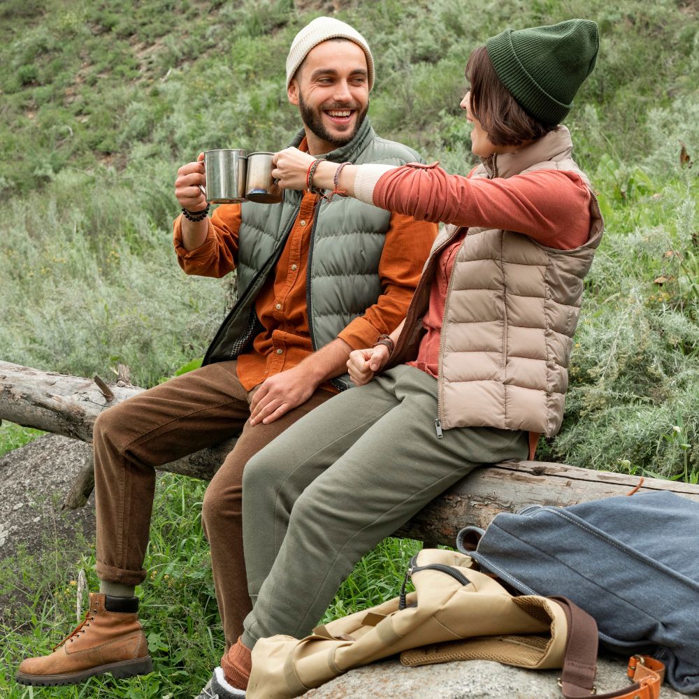 Two people sitting on a log in a natural setting, enjoying a warm beverage.
