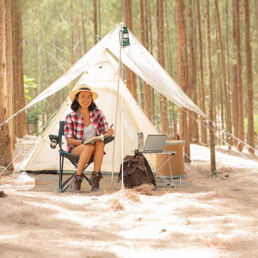 Woman sitting in a chair outside a tent in a forest setting